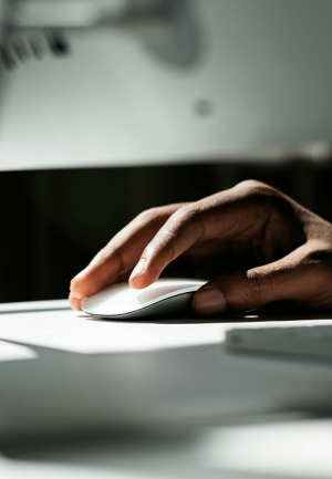 A close-up of a hand using a computer mouse in a softly lit office environment. 